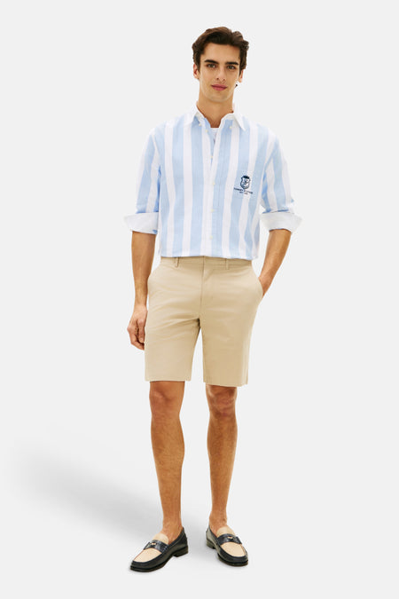 Bermuda beige de Tommy Hilfiger, porté avec une chemise rayée bleu et blanche et des mocassins.