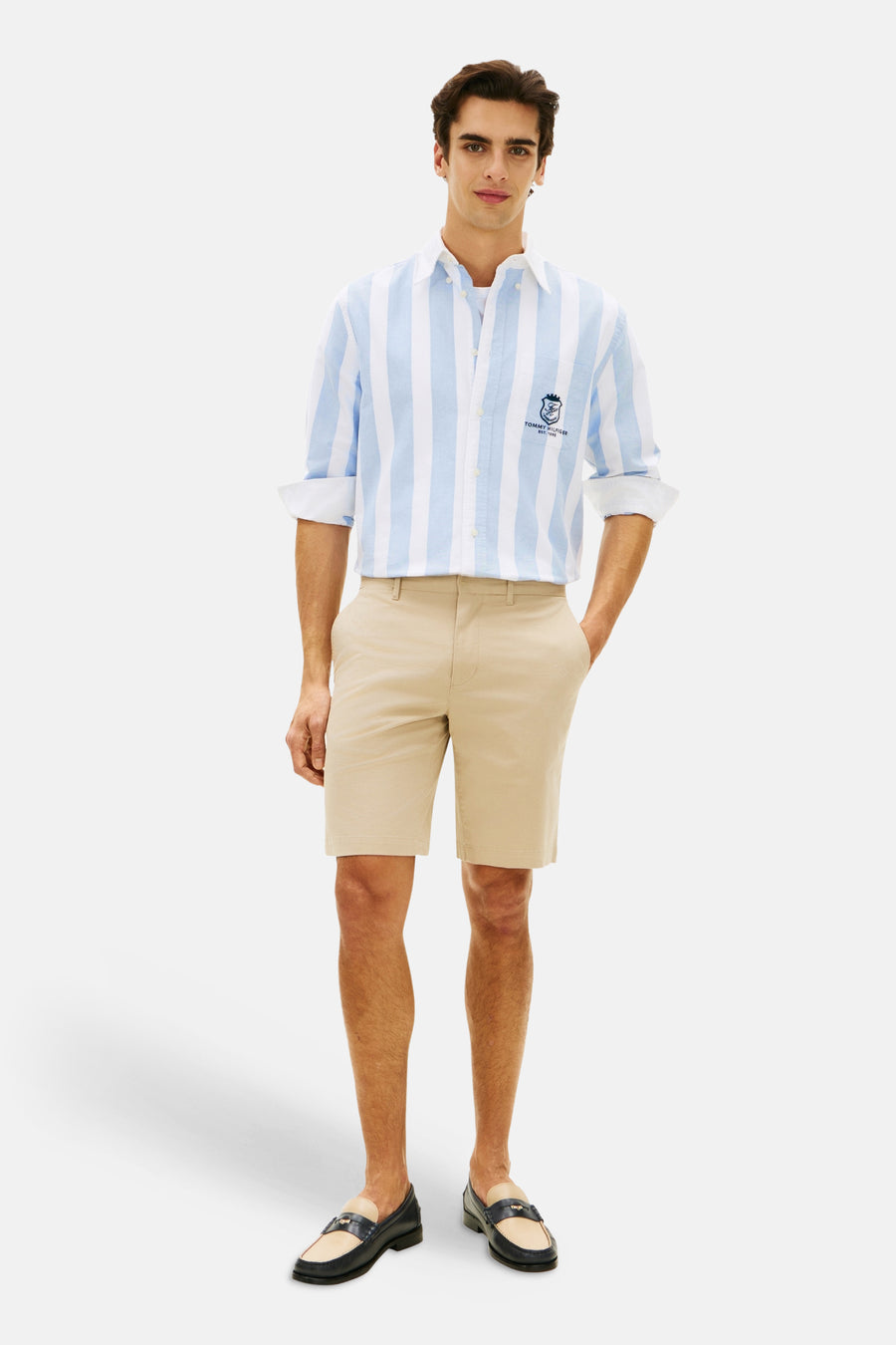 Bermuda beige de Tommy Hilfiger, porté avec une chemise rayée bleu et blanche et des mocassins.