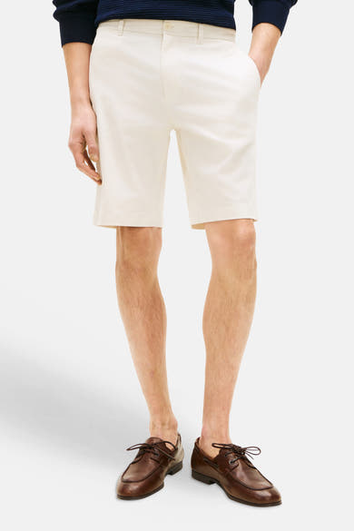 Bermuda écru de TOMMY HILFIGER porté avec un pull bleu marine et des chaussures bateau marron.