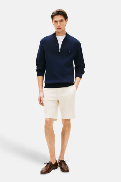 Bermuda écru de TOMMY HILFIGER, porté avec un pull bleu marine et des chaussures bateau marron.