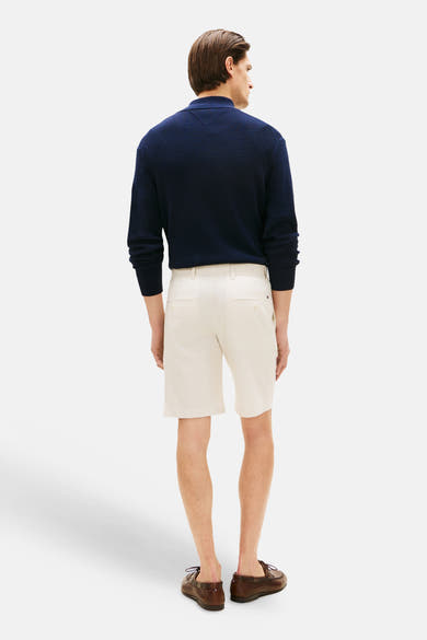 Bermuda écru de TOMMY HILFIGER, porté avec un polo bleu marine et des chaussures bateau marron.

