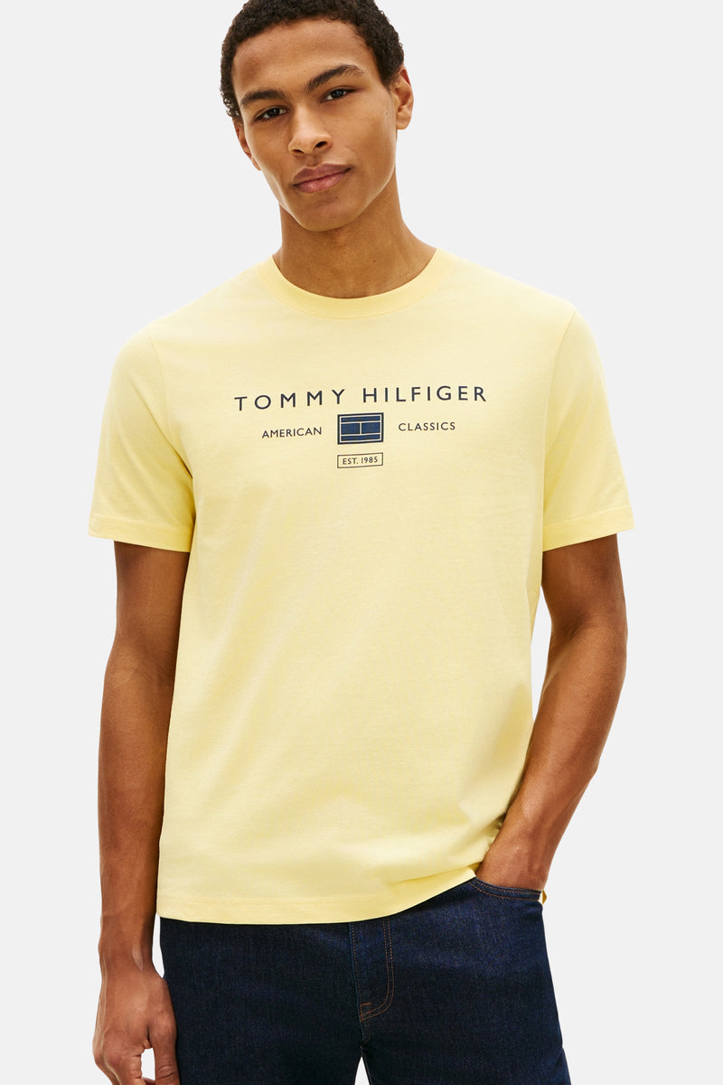 Gele T-shirt met korte mouwen van TOMMY HILFIGER, met opgedrukt logo op de voorkant, gedragen met een blauwe jeans en loafers.