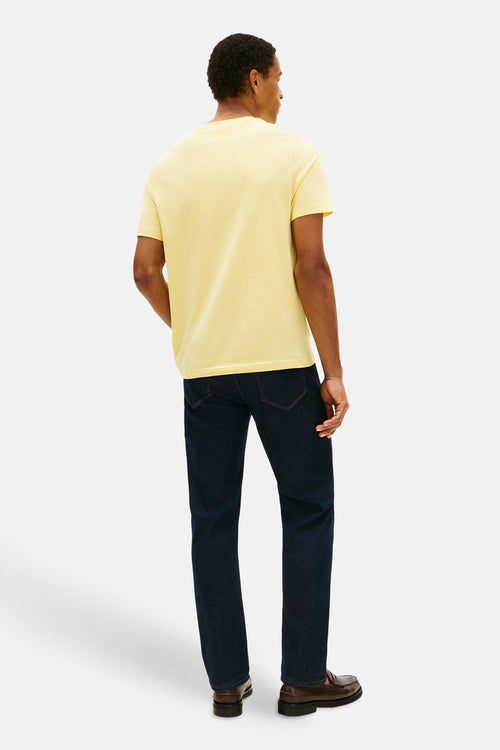 T-shirt jaune à manches courtes de TOMMY HILFIGER, porté avec un jean bleu foncé et des mocassins en cuir marron.