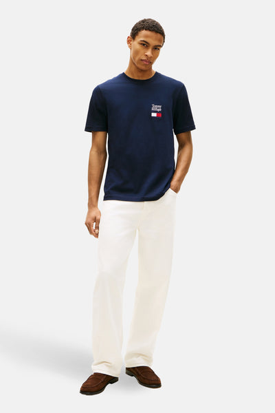 T-shirt à manches courtes bleu de TOMMY HILFIGER avec logo drapeau sur la poitrine, porté avec un pantalon blanc cassé.