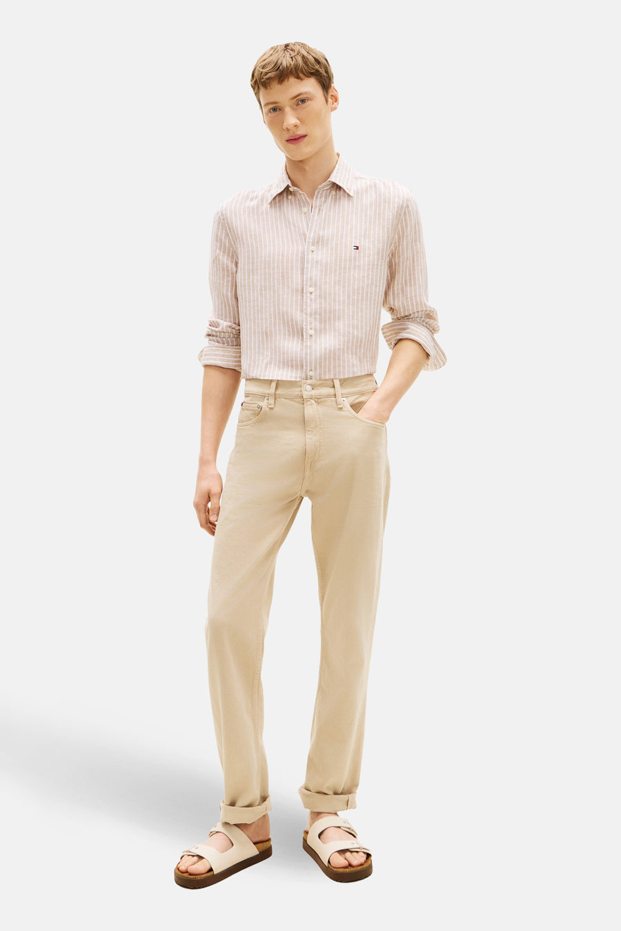 Chemise à manches longues beige à rayures, de TOMMY HILFIGER, portée avec un pantalon beige et des sandales.
