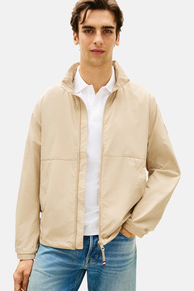 Veste beige de TOMMY HILFIGER, portée sur un polo blanc avec un jean bleu.