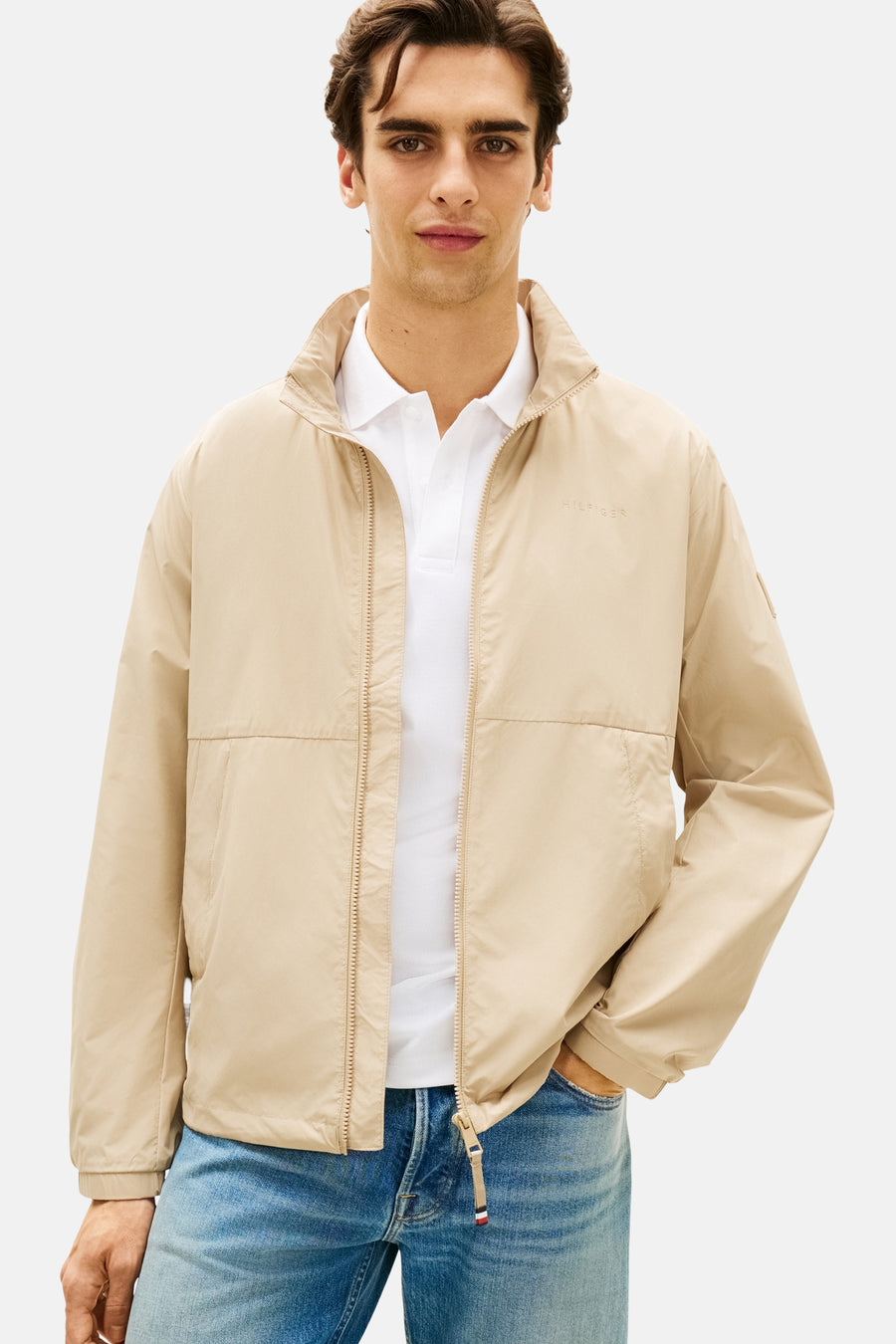 Veste beige de TOMMY HILFIGER, portée sur un polo blanc avec un jean bleu.