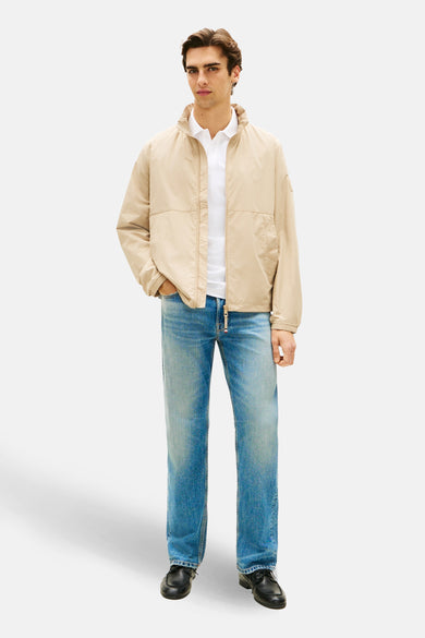 Veste beige de TOMMY HILFIGER, portée avec un polo blanc et un jean décontracté, sur fond uni.