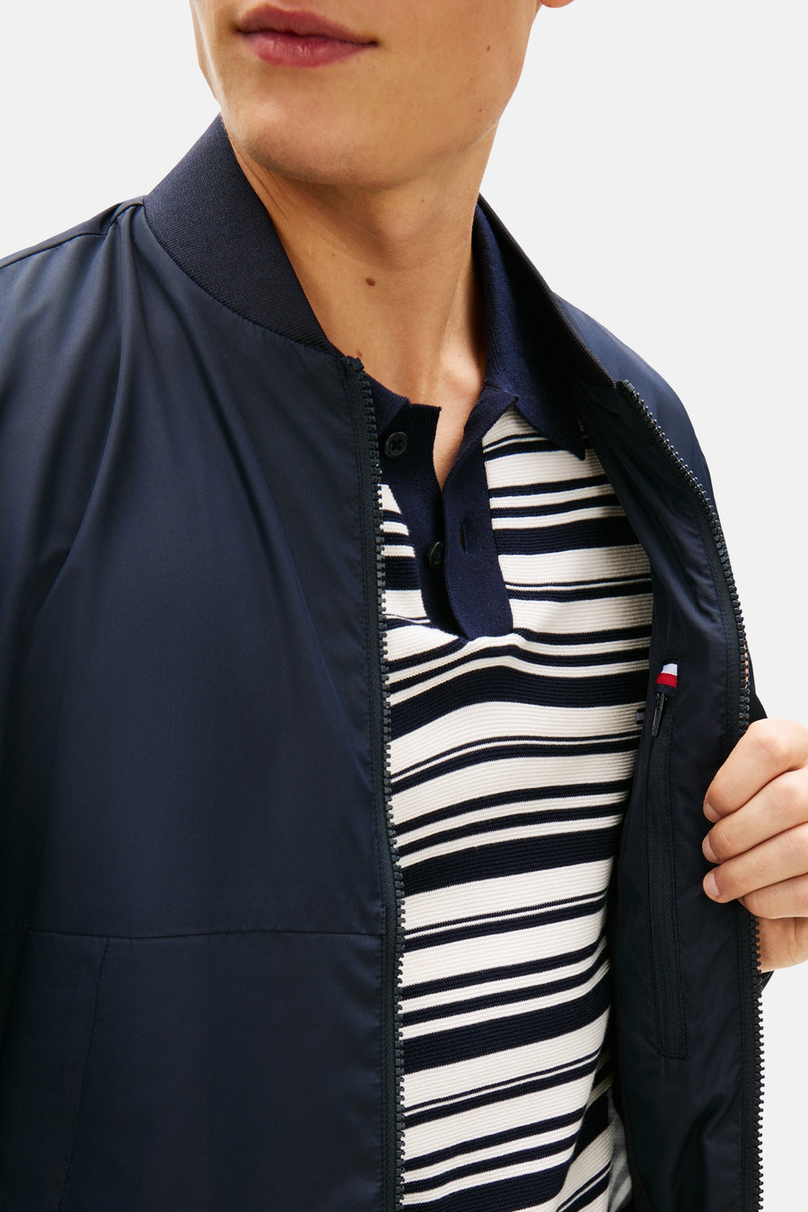 Veste bleue de TOMMY HILFIGER, ouverte pour révéler un polo rayé et une poche zippée.
