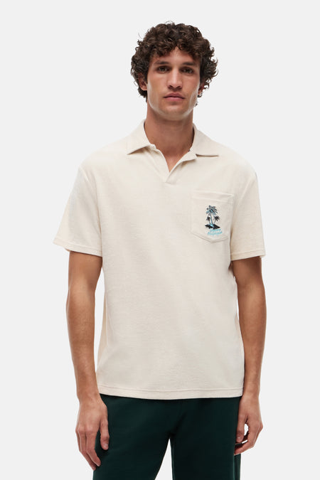 Ecru poloshirt van badstof van TOMMY HILFIGER met palmboomprint en script op de borstzak, gedragen door een man.
