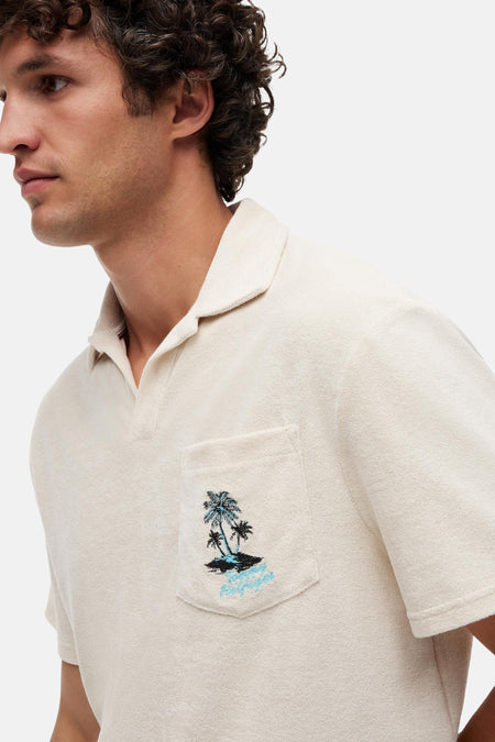 Polo écru en tissu bouclette de TOMMY HILFIGER avec motif palmiers et script sur la poche poitrine, porté par un homme.