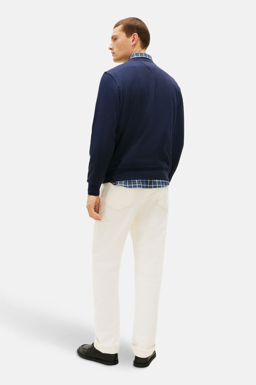 Sweat-shirt bleu de TOMMY HILFIGER avec un col rond, porté sur une chemise à carreaux et un pantalon écru.