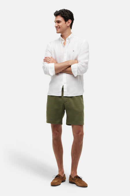Bermuda vert par Tommy Hilfiger, porté avec une chemise blanche et des chaussures bateau marron.