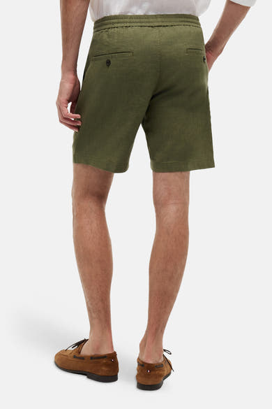 Bermuda vert en coton par Tommy Hilfiger, avec poches arrière boutonnées, porté avec des chaussures bateau marron.