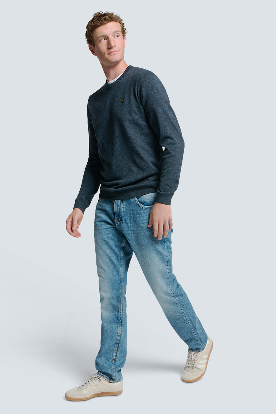 Pull à col rond bleu de NO EXCESS, porté avec un jean clair et des baskets beiges.