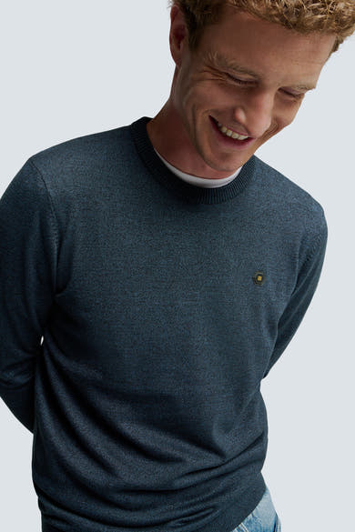 Pull à col rond bleu chiné de NO EXCESS, avec écusson à motifs géométriques, porté avec un t-shirt blanc.
