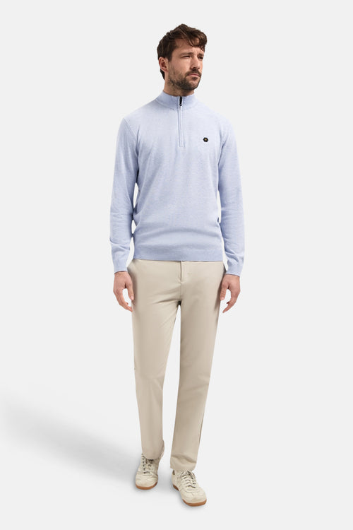 Blauwe trui met opstaande kraag van NO EXCESS, met korte ritssluiting en zwart logo op de borst, gedragen met een beige broek en witte sneakers.
