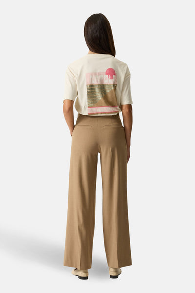 T-shirt à manches courtes beige de GARCIA, avec motif graphique dans le dos, porté avec un pantalon taille haute marron.
