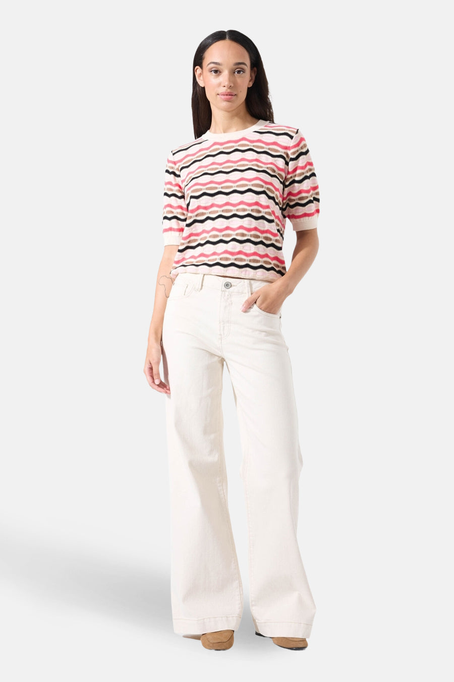 Pull à col rond multicolore de GARCIA, à rayures ondulées roses, noires et marron, porté avec un pantalon écru large.
