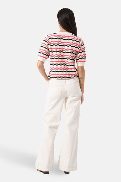 Pull à col rond multicolore de GARCIA, motif à rayures ondulées, porté avec un pantalon blanc évasé.