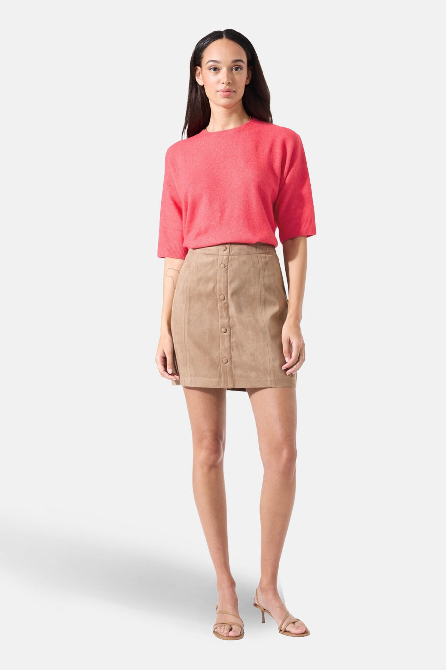 Pull à col rond rose de GARCIA, porté avec une jupe marron boutonnée et des chaussures à talons bas.
