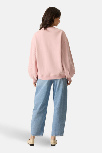 Sweat rose de GARCIA, manches bouffantes, porté avec un jean bleu ample et des mocassins beiges, vue de dos.
