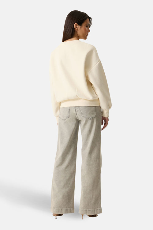 Sweat écru de GARCIA, coupe décontractée, porté avec un jean gris ample et des chaussures à talons marron.