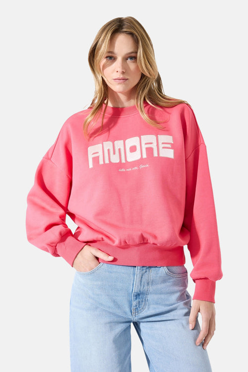 Sweat rose col rond de GARCIA, avec inscription décorative "Amore" sur le devant, porté avec un jean bleu clair.