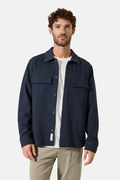 Chemise à manches longues bleue de GARCIA, avec poches poitrine et fermeture boutonnée sur un t-shirt blanc et un pantalon beige.