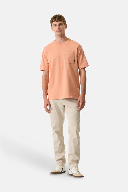 Chino écru de GARCIA, porté avec un t-shirt orange à poche et des baskets blanches.
