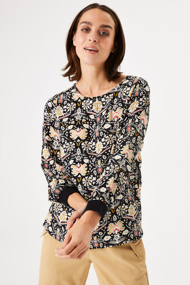 Blouse noire à motifs floraux by GARCIA, manches trois-quarts avec poignets noirs, portée avec un pantalon beige.