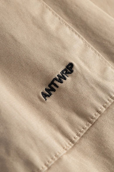 Pantalon beige de ANTWRP, avec une broderie du nom de la marque, détail de couture visible.