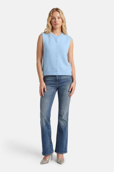 Blauwe bodywarmer van AMELIE ET AMELIE, mouwloos met knopen, gedragen met een spijkerbroek en zilveren pumps.
