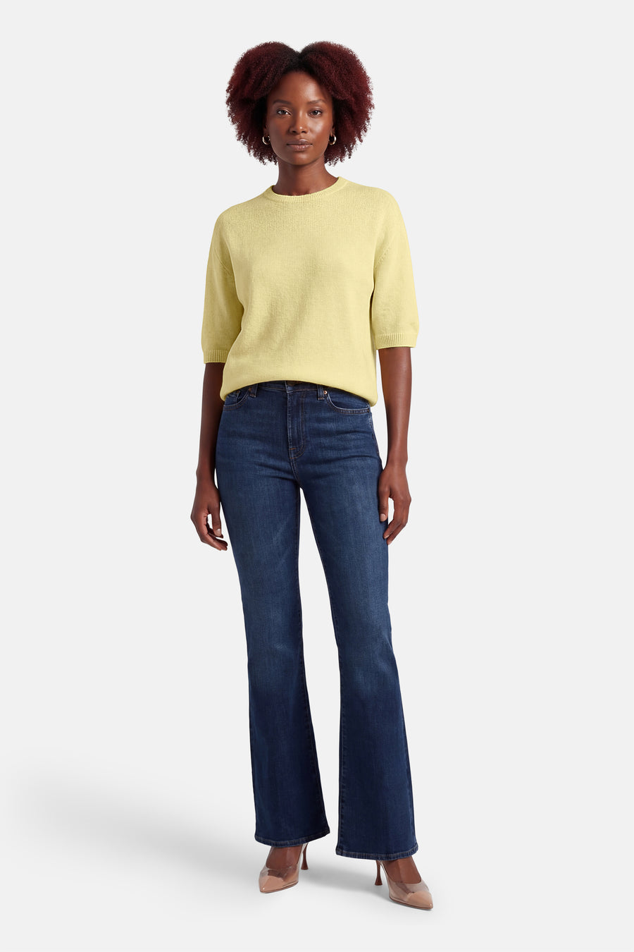 Gele rondehals trui van AMELIE ET AMELIE, korte mouwen, gedragen met een blauwe jeans en beige pumps.