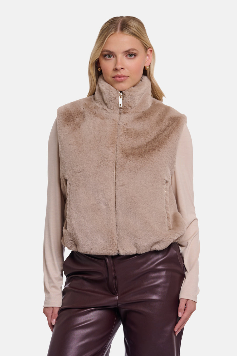 Beige faux fur bodywarmer by RINO PELLE, high collar with front zipper, worn over beige top and brown leather pants, front view