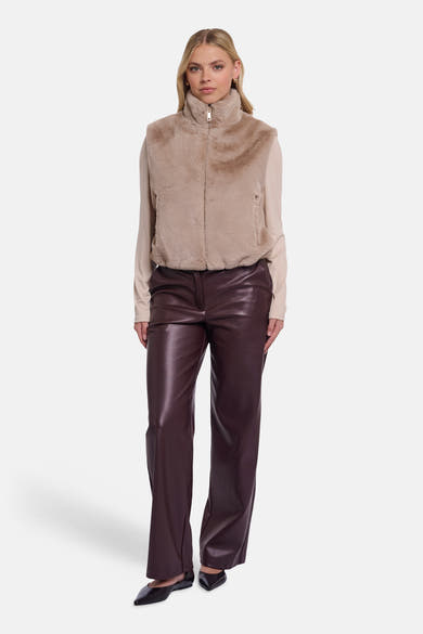 Beige faux shearling bodywarmer by RINO PELLE, high collar with front zipper, worn over beige top and dark brown leather pants, full-length front view
