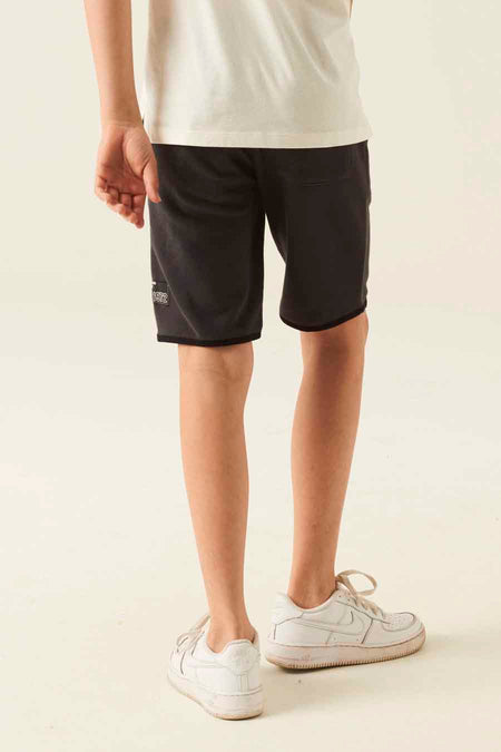 Dark gray cotton jogger shorts with side pocket and small patch detail, worn with white t-shirt and sneakers, back view.