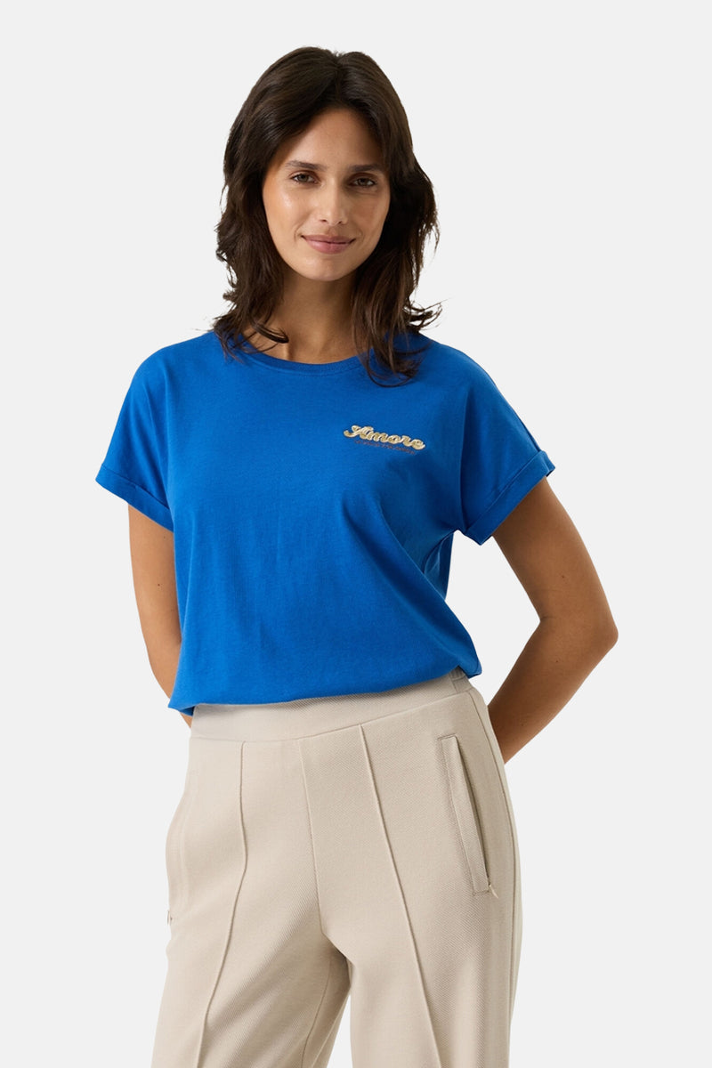 T-shirt bleu à manches courtes de GARCIA, orné d'un motif brodé « Amore », porté avec un pantalon beige.