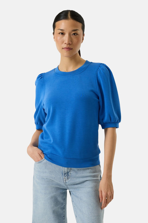 Sweat-shirt col rond bleu de GARCIA, avec manches bouffantes et ourlet côtelé, porté avec un pantalon en denim clair.
