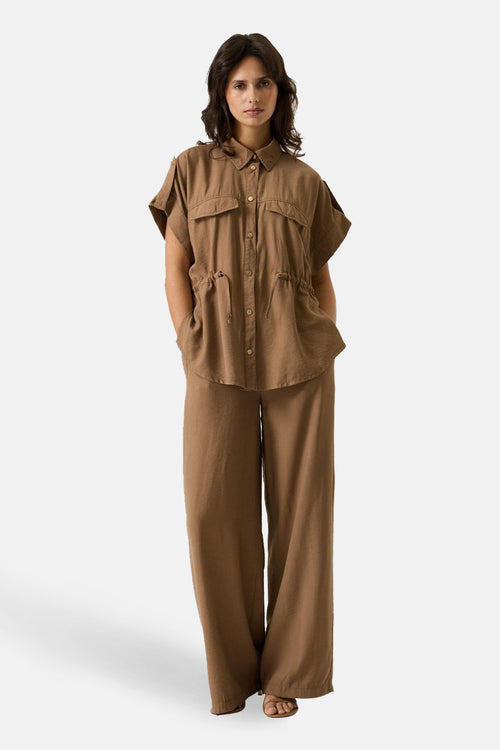 Pantalon taupe de GARCIA, jambes larges et coupe droite, porté avec une chemise marron assortie.
