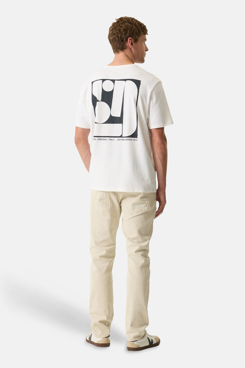 T-shirt blanc à manches courtes de GARCIA, avec un motif graphique noir au dos, porté avec un pantalon beige et des baskets.
