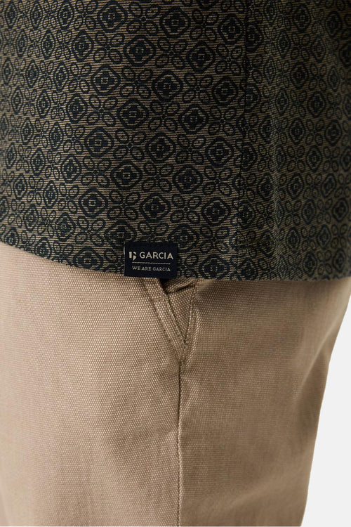 T-shirt à manches courtes vert, de GARCIA, avec motif géométrique noir sur le haut et pantalon beige uni.