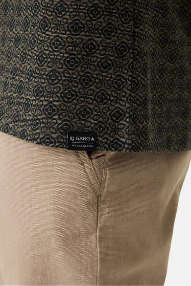 T-shirt à manches courtes vert, de GARCIA, avec motif géométrique noir sur le haut et pantalon beige uni.