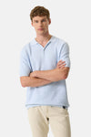 Polo en tricot bleu clair de GARCIA, porté avec un pantalon beige, bras croisés.