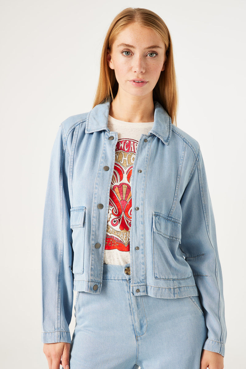 Veste en denim bleu clair de GARCIA, avec des poches à rabat et boutons métalliques, portée sur un t-shirt imprimé.
