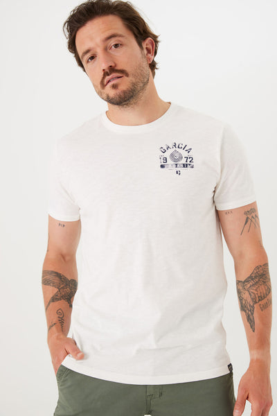 T-shirt blanc à manches courtes de GARCIA, avec motif imprimé sur la poitrine, porté avec un pantalon kaki.
