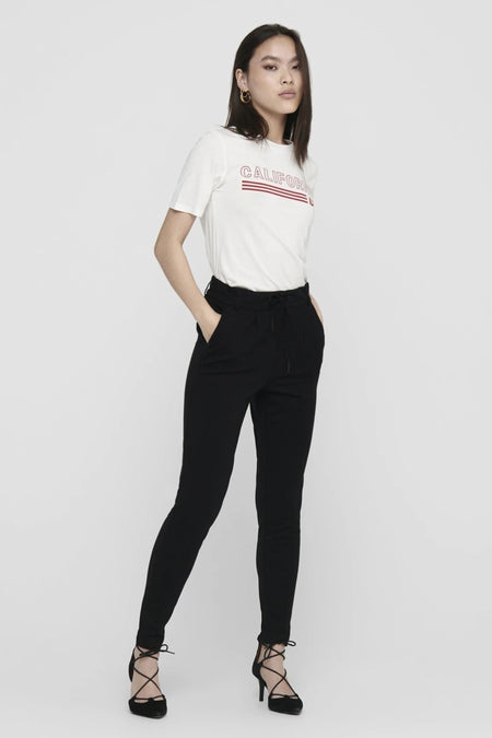 Jogging noir par ONLY®, porté avec un t-shirt imprimé et des chaussures à talons lacées.