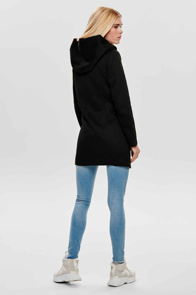 Veste longue noire de ONLY, avec capuche, portée avec un jean bleu clair et des baskets compensées.