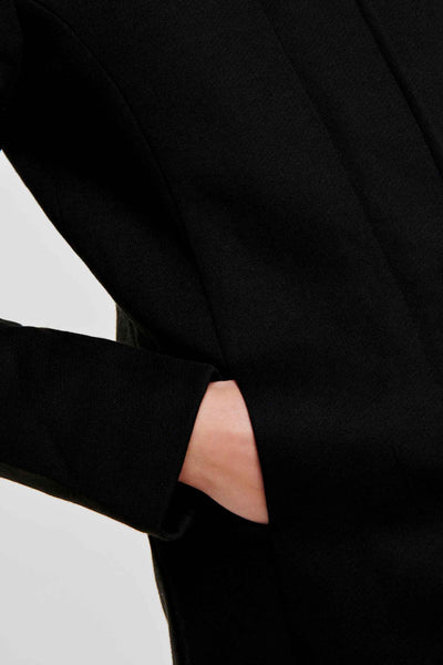 Veste longue noire de ONLY, avec une main dans la poche.