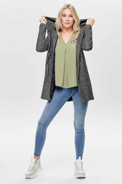 Veste longue grise de ONLY, portée avec un chemisier vert et un jean bleu, chaussures de sport blanches.